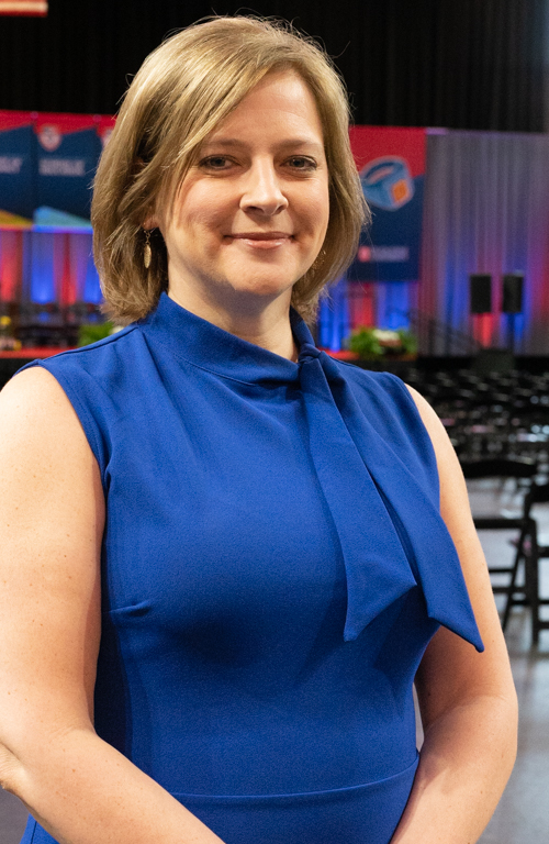Education alum Dr. Kara Eckert smiling on School of Education Commencement floor with the stage behind her.